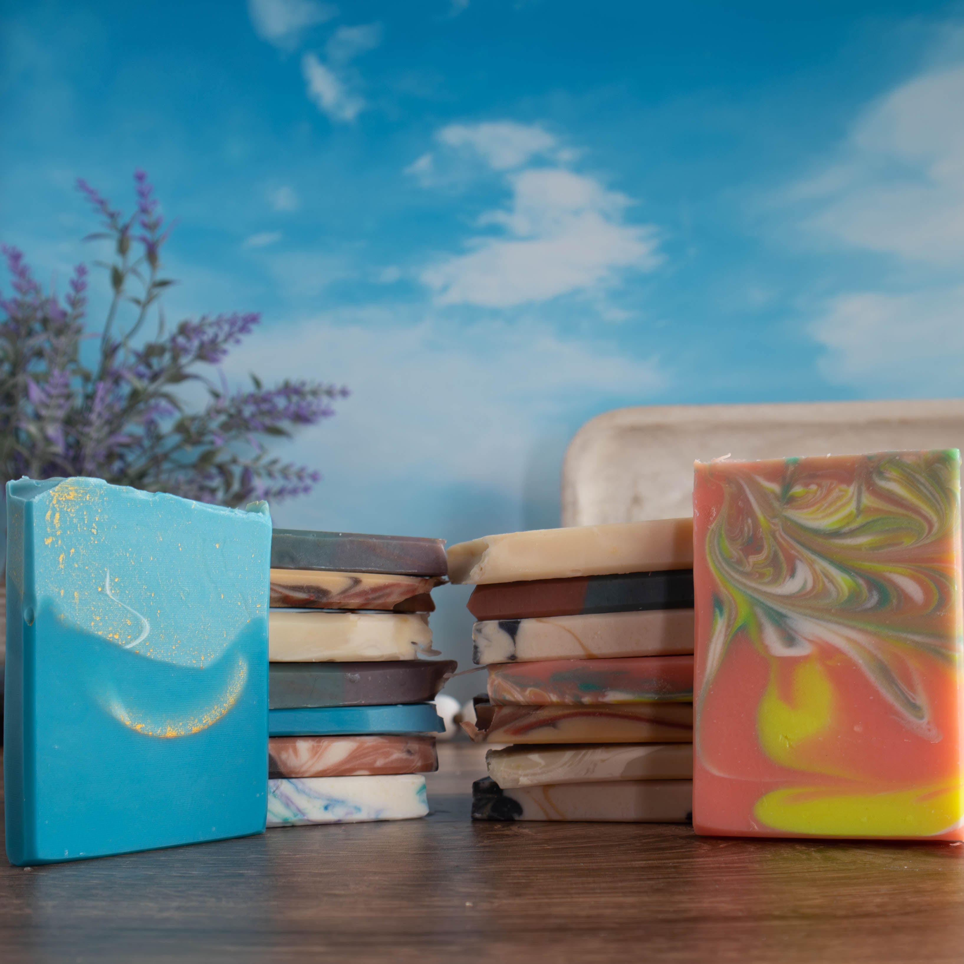 there are 14 different soap samples, 7 are stacked on top of each other facing another 7 stacked soap ends. There is another soap end  standing off to the side of each stack to show the face. There is a pretty blue sky in the background 