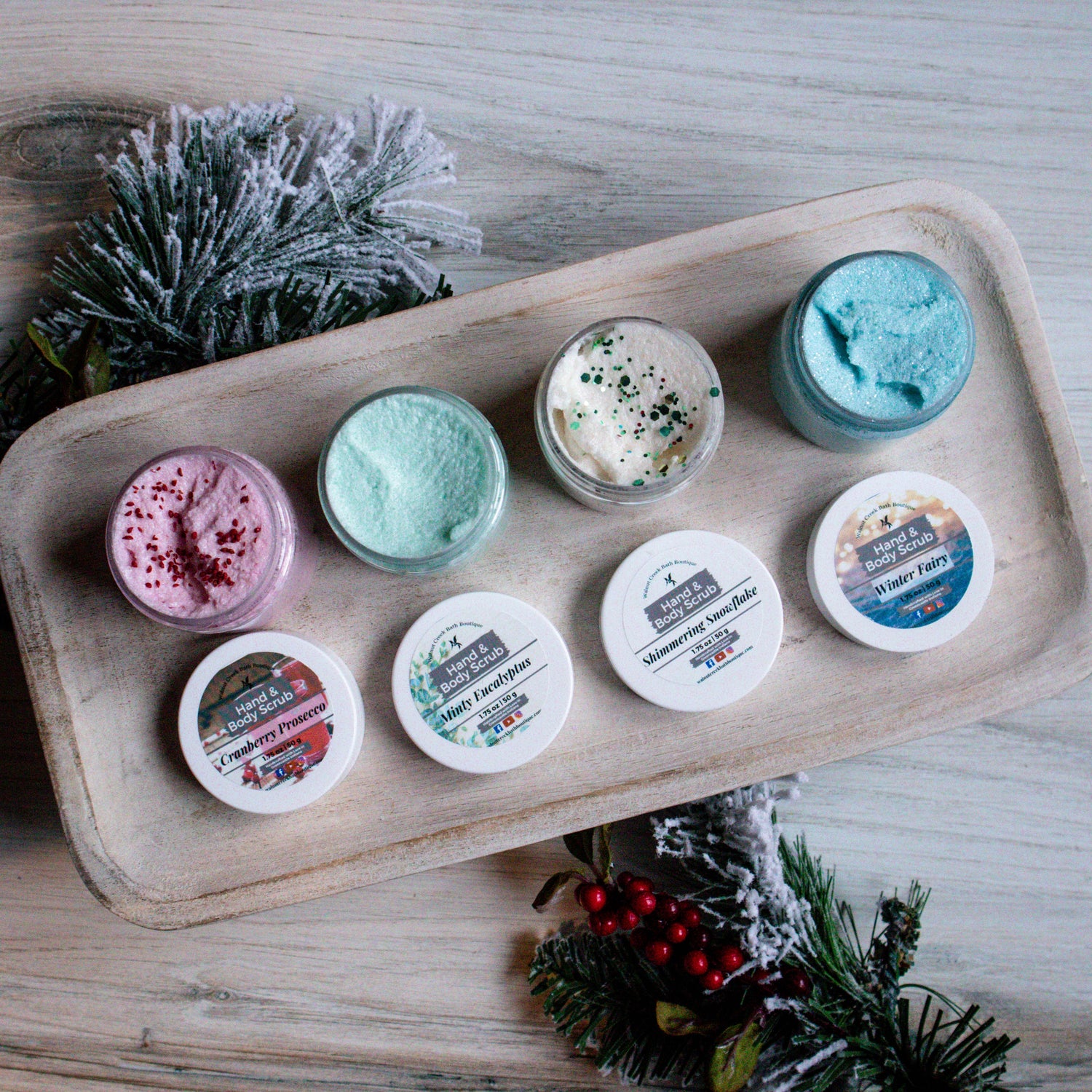 all four scrubs lined up open sitting on a shelf. the tops are in front of each of them. this shows the inside of the jars. there is christmas greenery that is frosted splayed underneath the shelf