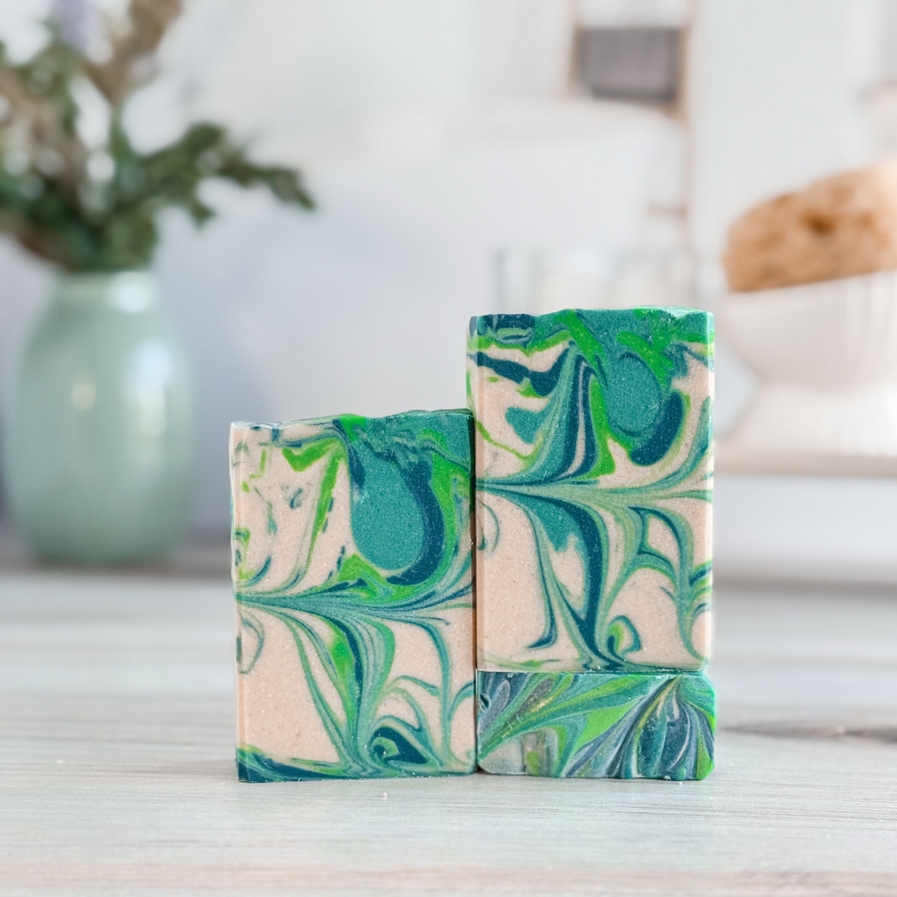 Three marbled soap bars with green and blue patterns on a wooden surface.