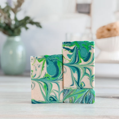 Three marbled soap bars with green and blue patterns on a wooden surface.