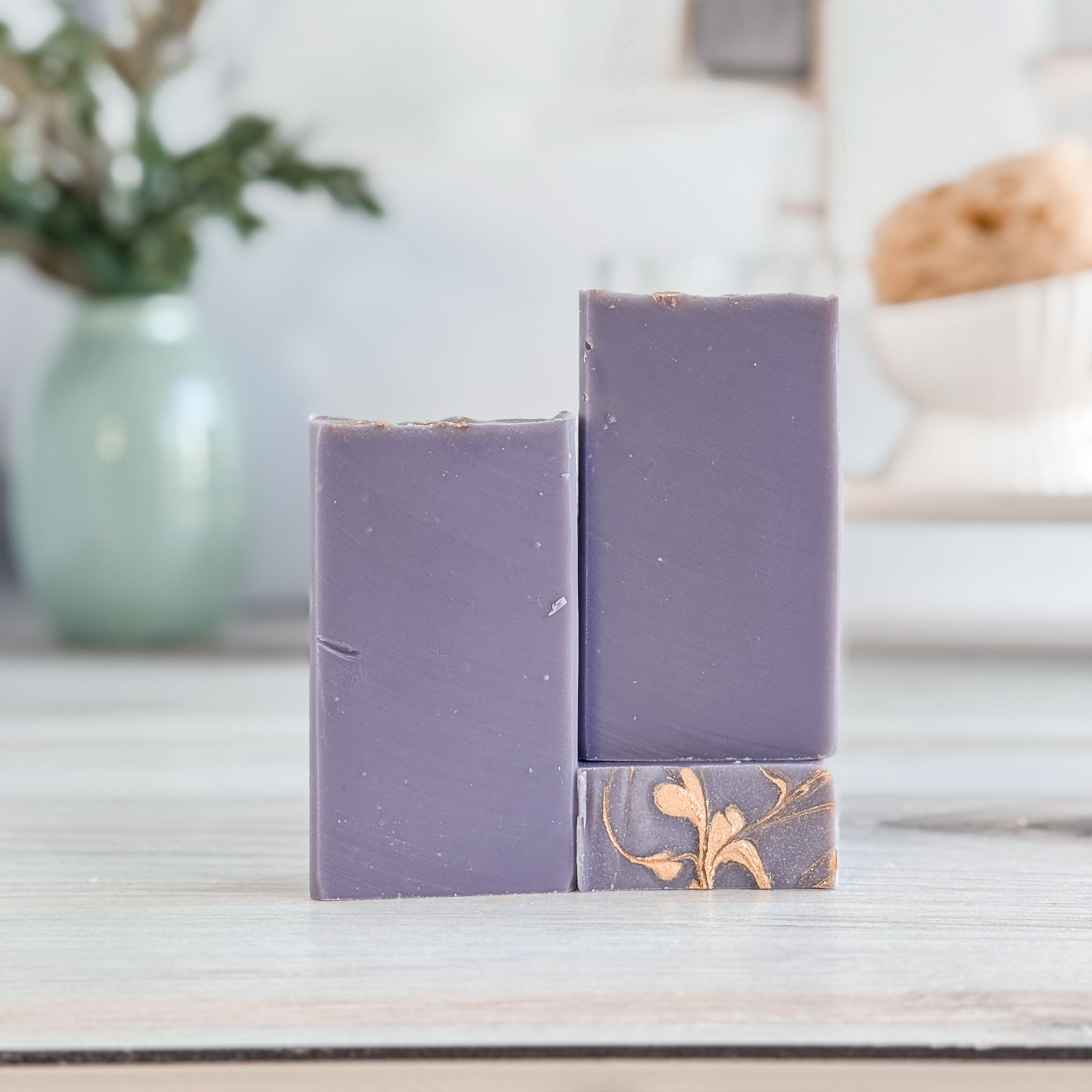 Tthree purple soap bars with floral design on a white surface, blurred background