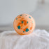 Round orange object with blue specks on a white fabric background