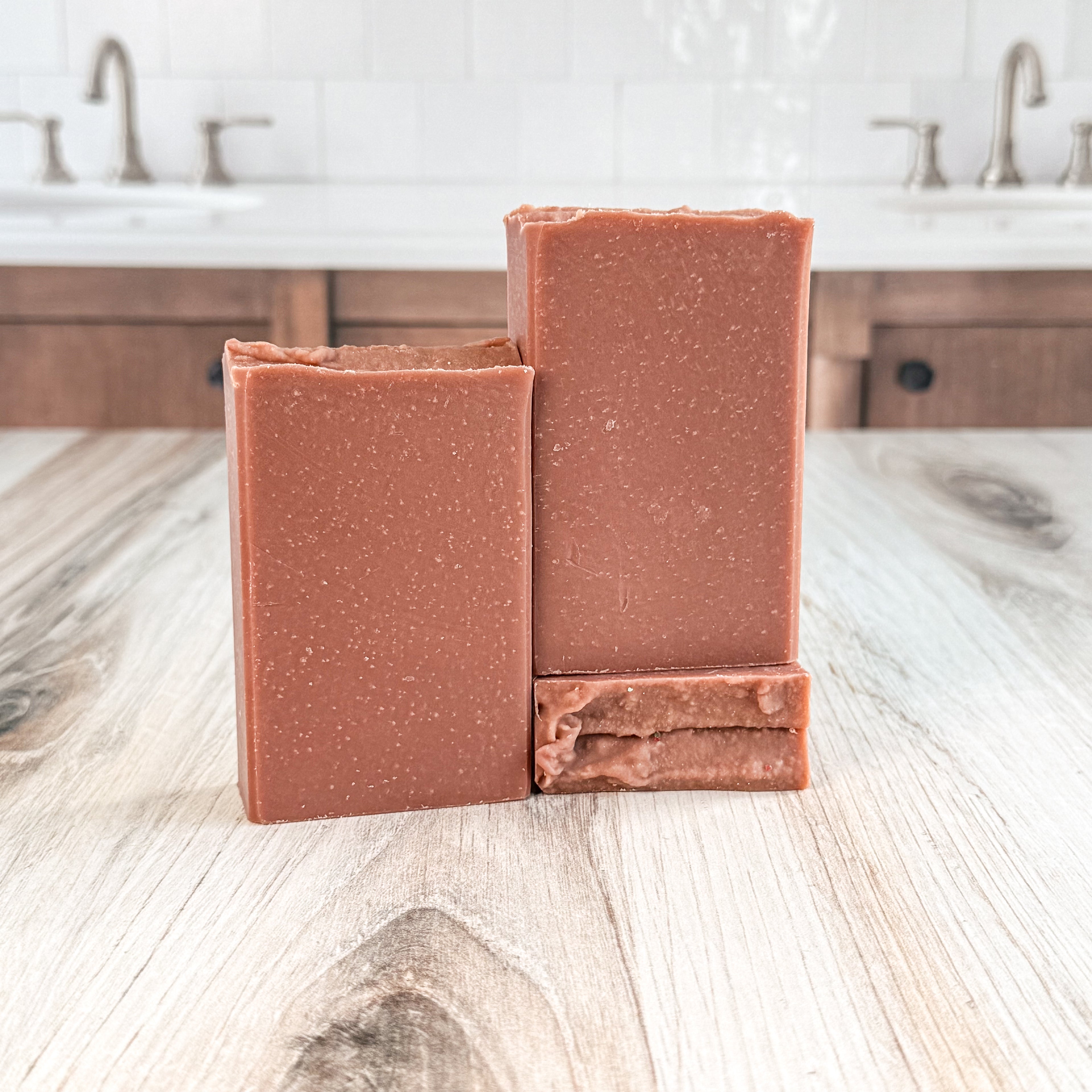 Two brown soap bars on a wooden surface with a blurred bathroom background