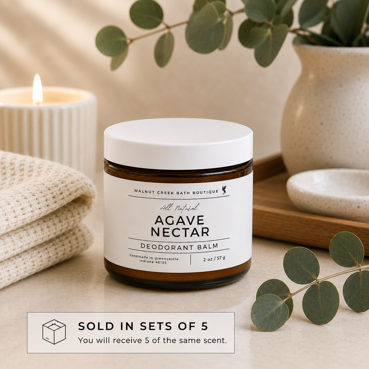 Agave Nectar deodorant balm jar with candle and eucalyptus leaves on a neutral background