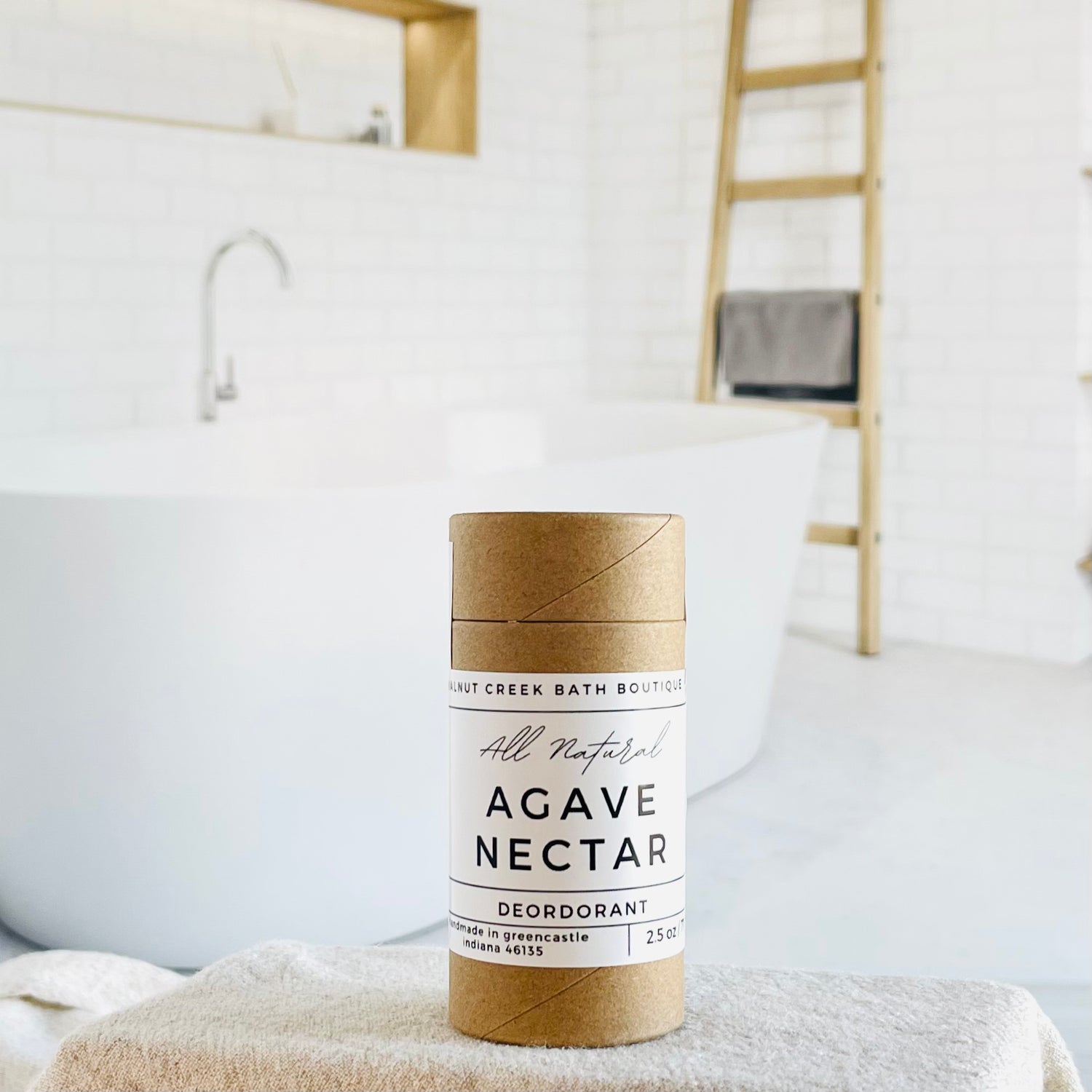 agave nectar deodorant is shown, the label is minimalist in design, white with black lettering. in the background is a spa like bathroom