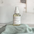 Bottle of Apple Cider + Oak room spray on a green fabric surface with a neutral background