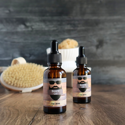 2 beard oil bottles are shown with one slightly more forward than the other. the label shows a bearded outline of a man with sunglasses on. there is a wood base that these are sitting on with a dark black/grey wood background. in the background is a body brush and a loofah on a tray.