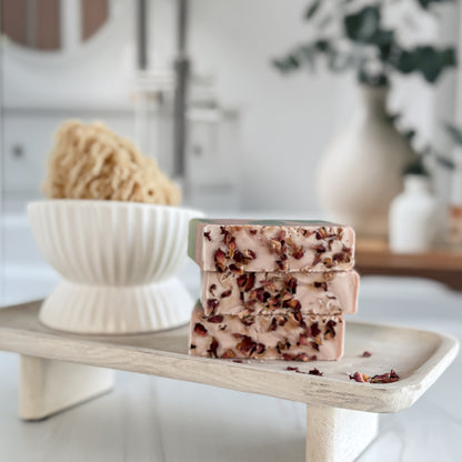 Stack of soap bars with natural ingredients on a wooden stand in a bathroom setting.