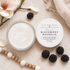 Goat milk cream jar with blackberries and flowers on a textured surface