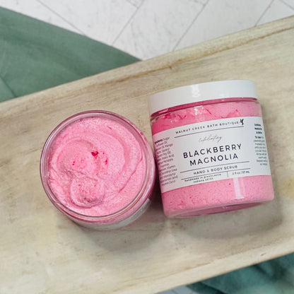 Blackberry Magnolia scrubs with one laying flat and the other next to it with the top off to show the pink scrub inside of the jar