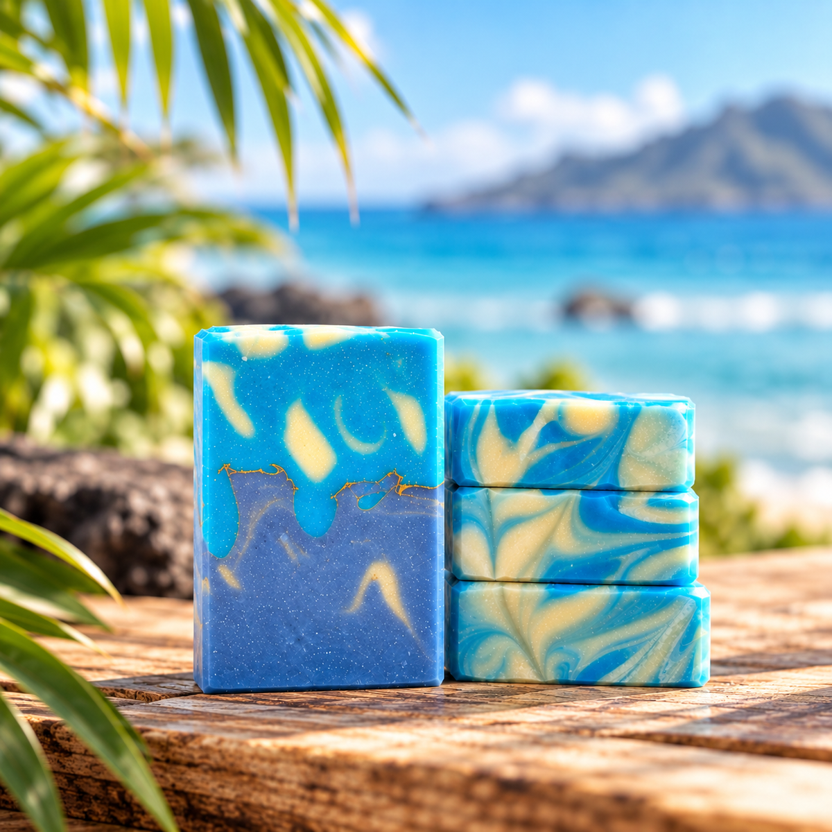 Three handmade rectangular bars of soap with blue and cream swirls, displayed on a rustic wooden table with a tropical beach and palm leaves in the background.