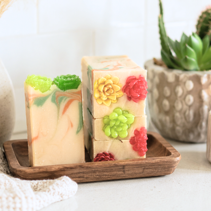 Decorative soap bars with floral designs on a wooden tray, with a plant in the background.