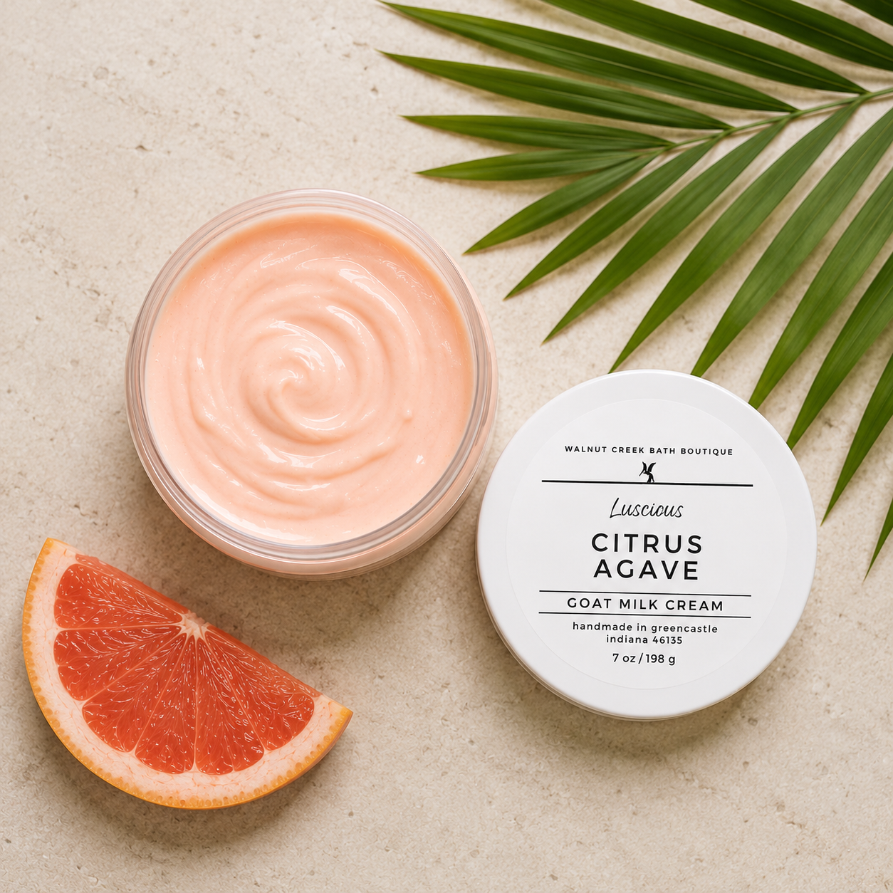 Jar of Citrus Agave goat milk cream with a slice of grapefruit and palm leaf on a beige background