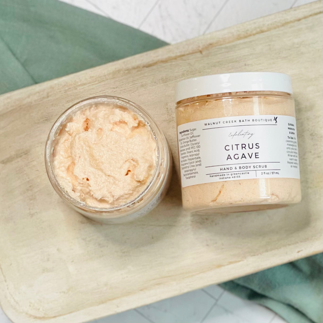 Citrus Agave scrubs with one laying flat and the other next to it with the top off to show the orange scrub inside of the jar