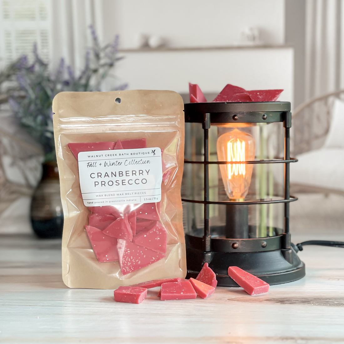 cranberry prosecco wax melt bag next to lit burner. there are wax melts on the table scattered about to shoe the pieces - these are red brittle pieces