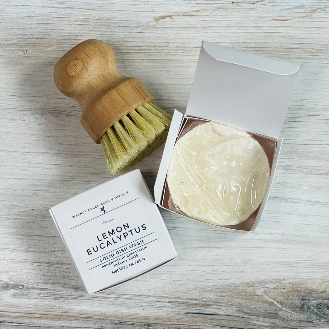 lemon eucalyptus dishwash shown in an open box, next to a closed box showing the label. there is a dish brush just to the top left of these boxes