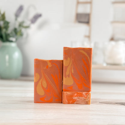 Three orange and pink marbled soap bars on a wooden surface with a blurred background