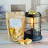 french toast wax melt bag is full and standing next to a rustic farmhouse type burner that is on and filled with the yellow/orange snap bar pieces of wax. there are also a few pieces of the snapped bar on the table in front of both to show the size and color of the pieces