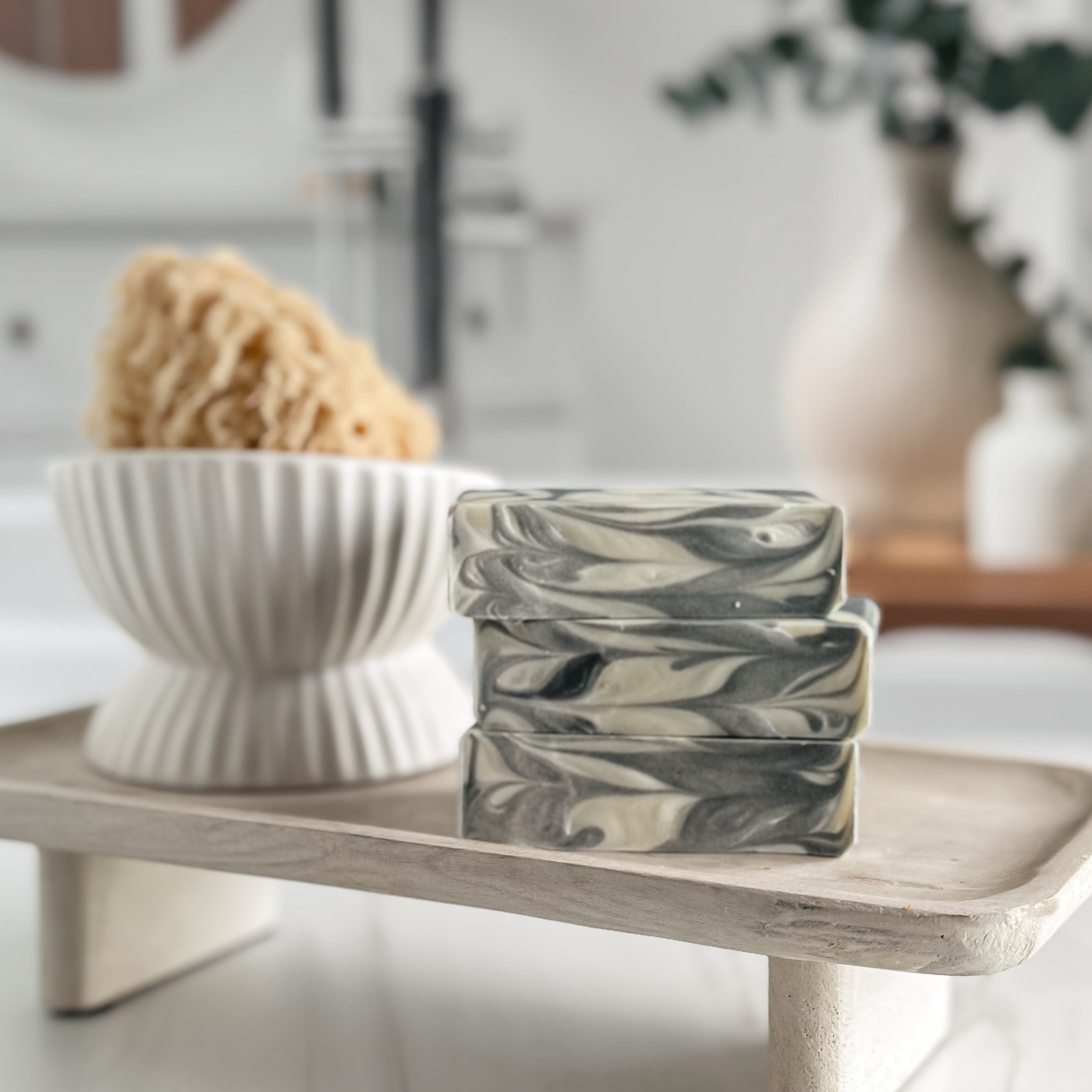 Marble-patterned soap bars on a wooden stand with a bowl of sponges in the background.