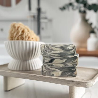 Marble-patterned soap bars on a wooden stand with a bowl of sponges in the background.