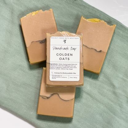 3 golden oats are laying flat on a green cloth with another on top of them showing the label.