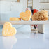 3 light orange harmony shampoo bars shaped in a heart. One is leaning on its side while the other two are on a trey, one leaning on the other. there is a loofah next to them with a cup of hair tools in the background