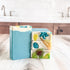 Stack of colorful soap bars on a wooden surface with a kitchen background