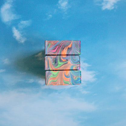 2 jad soaps are standing tall - your view is a top down view of the tops only. this shows the pretty swirls, mostly orange with some blue and pinks and a little green. they are sitting on a blue sky background that has whispy clouds.