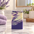 A rectangular handmade soap bar with a purple and cream marble swirl pattern, standing on a marble countertop with lavender and bath accessories in the background.