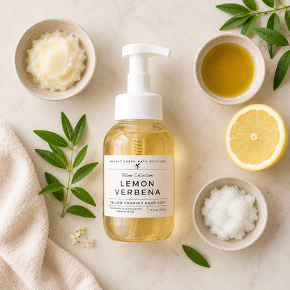 A bottle of Lemon Verbena hand soap by Monk Creek Bath Boutiques, styled in a flat-lay with bowls of ingredients (lemon, exfoliating scrub, oil, salt) and green leaves on a light beige textured background.