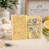 Three bars of pale yellow bath soap speckled with black poppy seeds, arranged on a light wood surface. A folded cream towel, a lemon slice, and a blurred background sign reading Walnut Creek Bath Boutique are visible.
