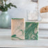 Two green and beige marbled soap bars on a wooden surface with a blurred background.