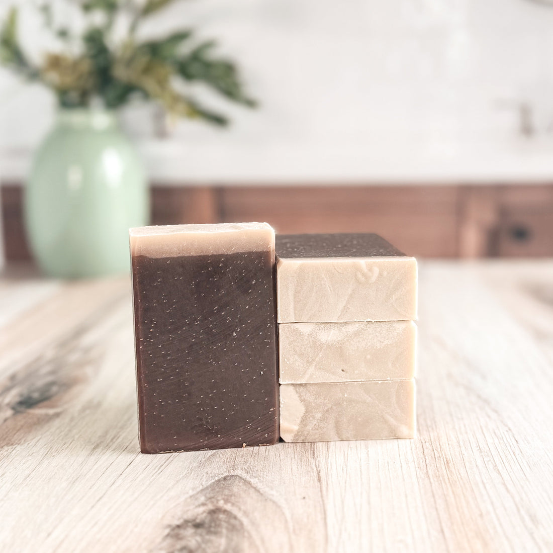 Two bars of soap, one brown and one beige, on a wooden surface with a blurred background.