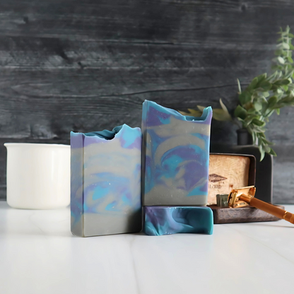 3 perfectly manly soaps are shown. they are grey with blue and purple swirls throughout. there is a gold old fashioned razor in the background