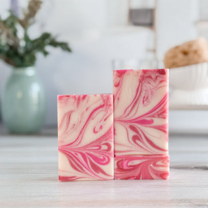 Two pink and white marbled soap bars on a wooden surface with a blurred background
