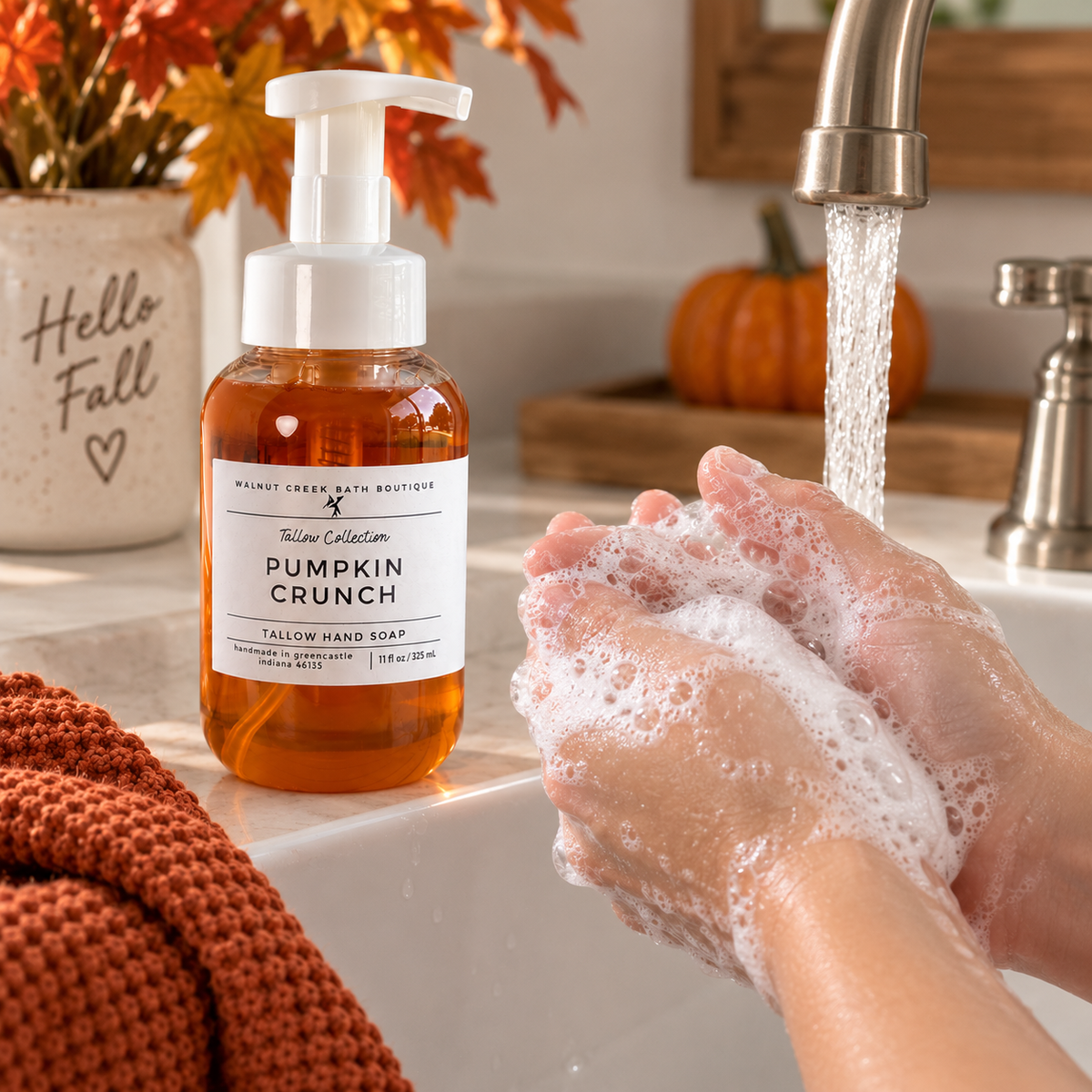 A bottle of Mount Creek Bath Boutique Fall Hand Soap labeled Pumpkin Crunch sits on a bathroom counter next to running water under a faucet, with a person&