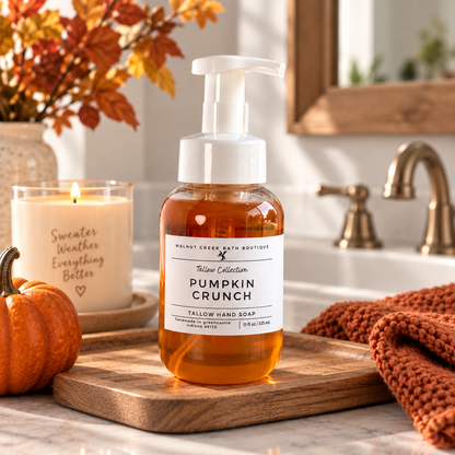 A bottle of Walnut Creek Bath Boutique Tallow Collection Pumpkin Crunch Tallow Hand Soap sits on a wooden cutting board in a warm, autumn-themed bathroom setting with a candle, small pumpkin, and knit blanket.