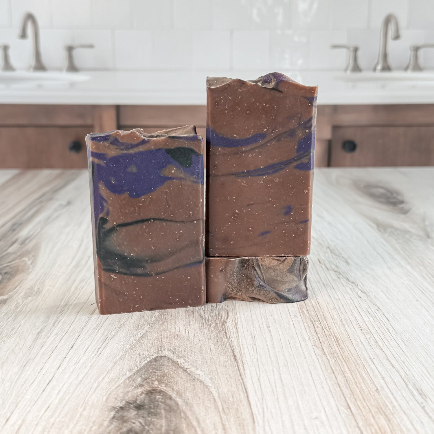 Two marbled soap bars on a wooden surface with a bathroom background.