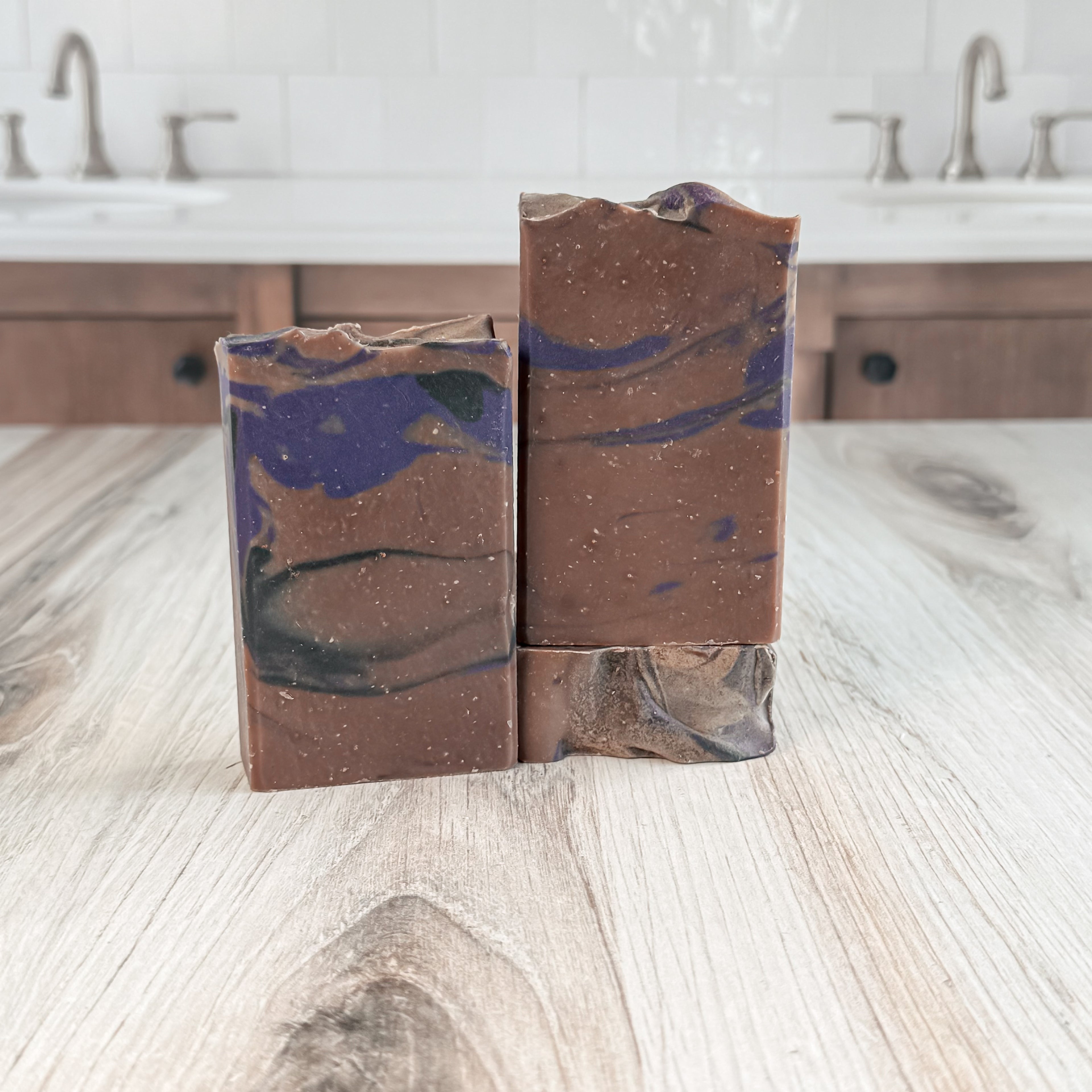 Two marbled soap bars on a wooden surface with a bathroom background.
