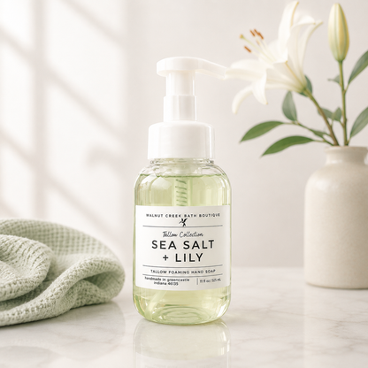 Walnut Creek Bath Boutique Sea Salt + Lily Tallow Foam Wash hand soap bottle on a marble countertop with a green cloth and white lilies in the background.