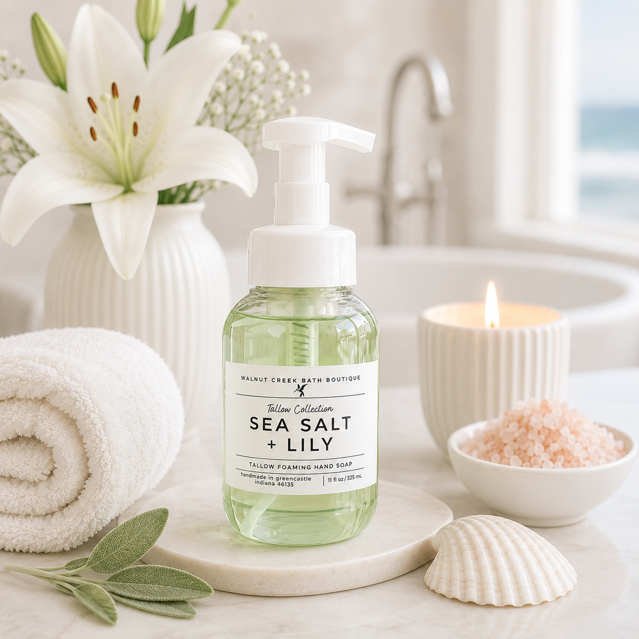 A bottle of Wald Creek Bath Boutique Sea Salt + Lily Calming Shampoo stands on a marble coaster in a bright bathroom setting. The scene includes a rolled white towel, a white lily flower in a vase, a lit candle, a bowl of pink salt, and a seashell.
