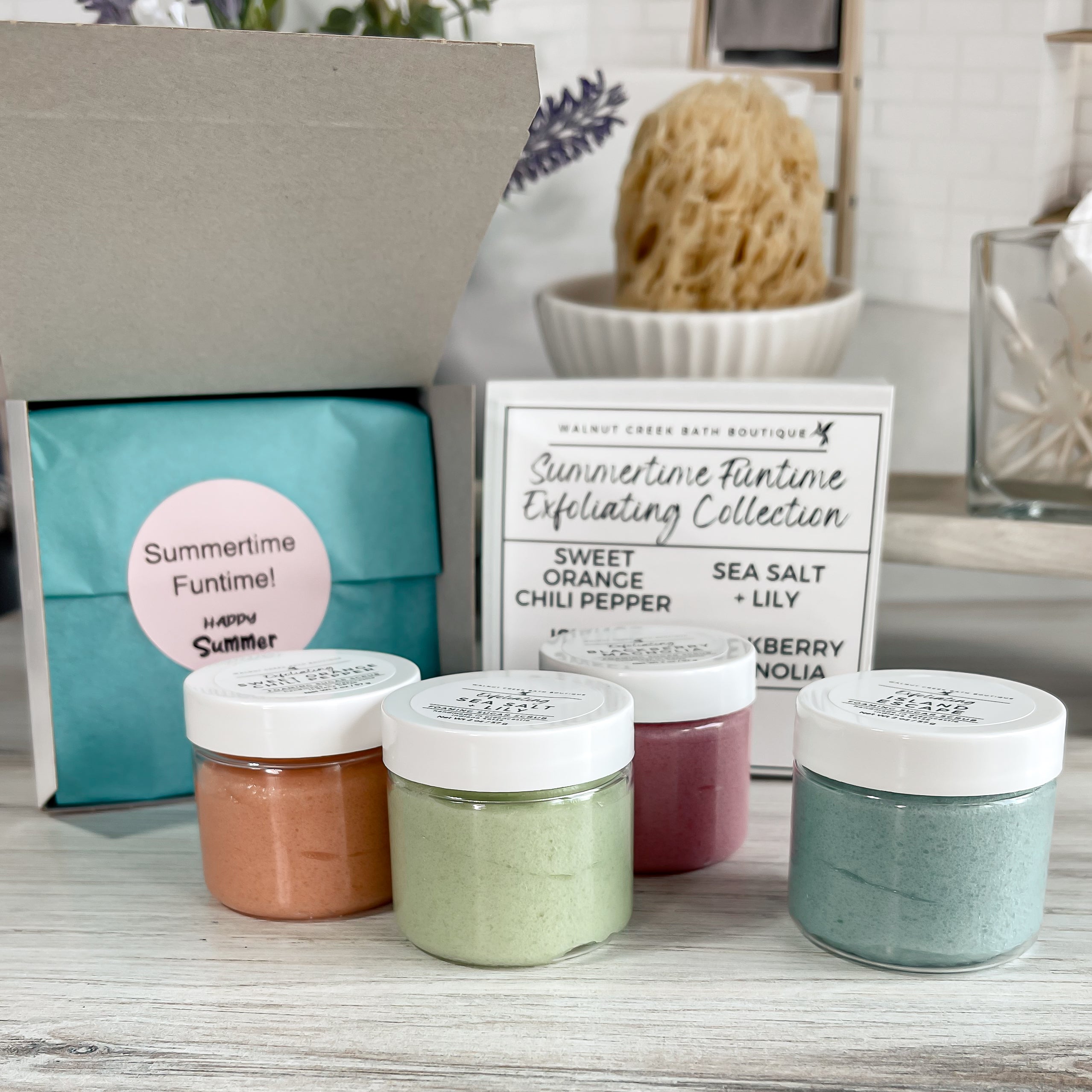 Four small jars with white lids on a wooden surface, with a branded box and sign in the background.
