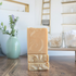 3 cedar leaf and lavender soaps are shown. 2 are laying flat to show the textured tops and one is standing on top of them to show the creamy swirl in the tan soap. in the background is a tray with glass dishes of q-tips and cotton balls, there is also a sage green vase with lavender buds in the background