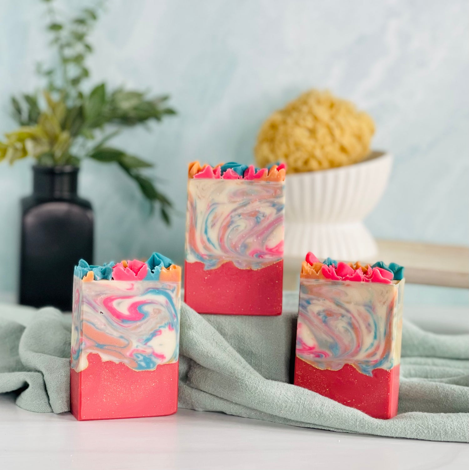 three day dreams soaps are shown with one on a sage green covered dias along with a loofah in a dish in the background