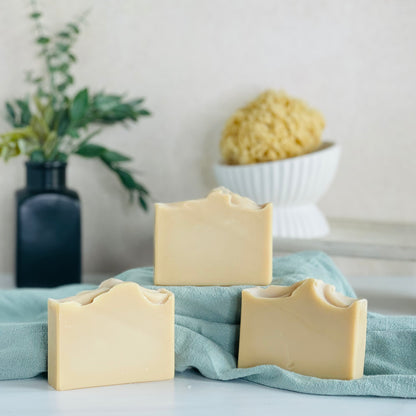 three patchouli sunrise soaps are shown with one on a sage green  covered dias along with a loofah in a dish in the background