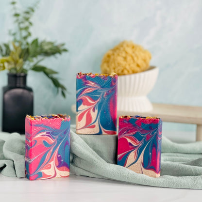 three green wildflower breeze soaps are shown with one on a sage green covered dias along with a loofah in a dish in the background