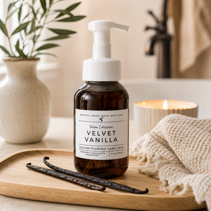 A bottle of Mount Green Bath Boutique Vanilla Collection Velvet Vanilla follow foaming hand soap sits on a wooden tray in a bathroom setting, surrounded by vanilla beans, a knit towel, and a lit candle.