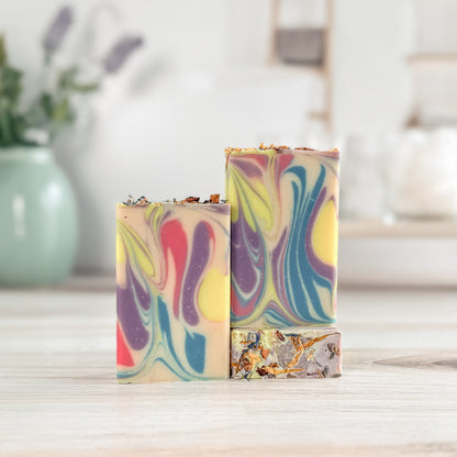 Two colorful swirled soap bars on a wooden surface with a blurred indoor background.