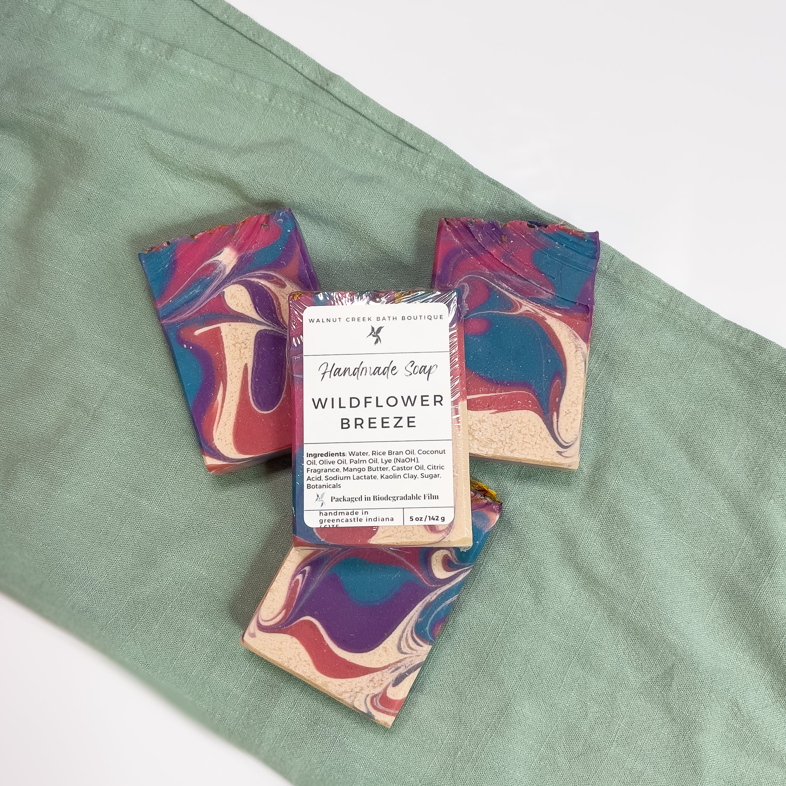 top down view of three wildflower breeze soaps to show the beautiful swirls of pink, blue and cream. another bar with the label is laying on top to show the simple white lable.