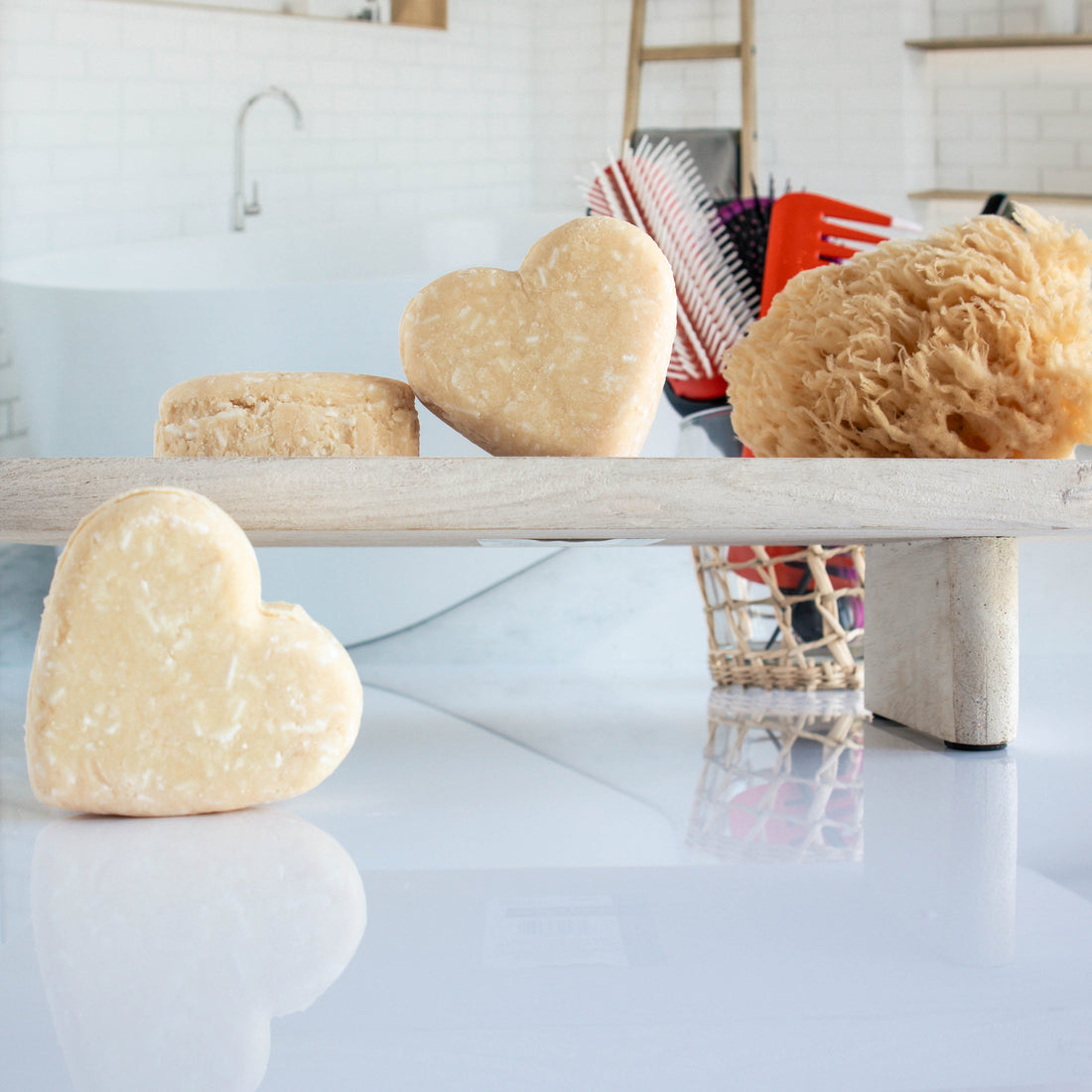 3 light yellow zesty cedarwood shampoo bars shaped in a heart. One is leaning on its side while the other two are on a trey, one leaning on the other. there is a loofah next to them with a cup of hair tools in the background